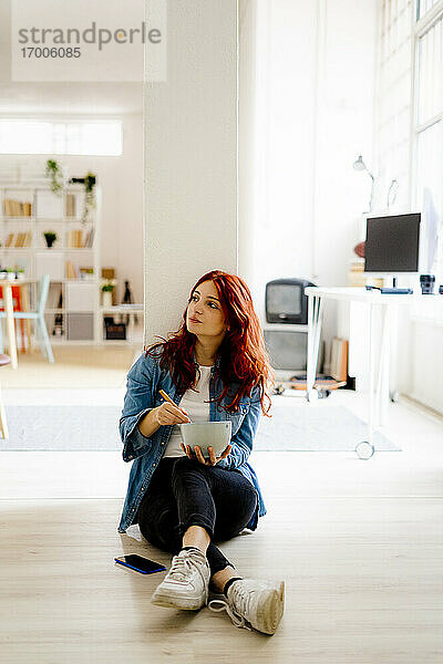 Geschäftsfrau isst Nudeln  während sie im Büro auf dem Boden sitzt