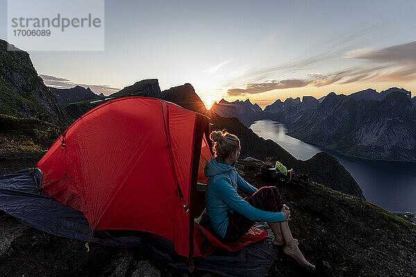 Frau bewundert die Aussicht  während sie im Lager auf dem Berg Reinebringen sitzt. Lofoten  Norwegen