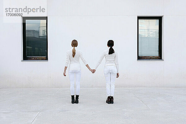 Junge Frauen halten sich an den Händen und stehen vor einem weißen Gebäude