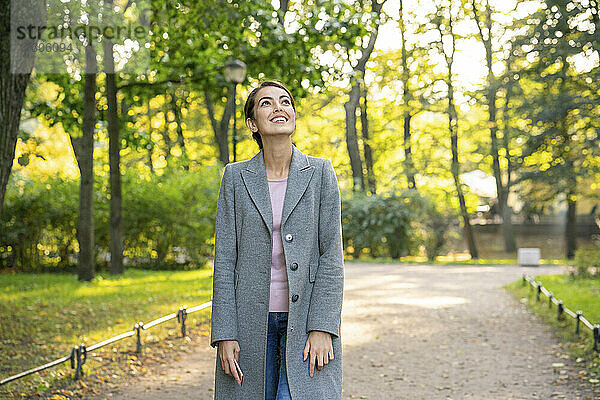 Lächelnde Geschäftsfrau  die beim Gehen im Park nach oben schaut