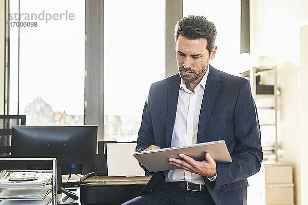 Geschäftsmann im Anzug  der ein digitales Tablet benutzt  während er im Büro sitzt