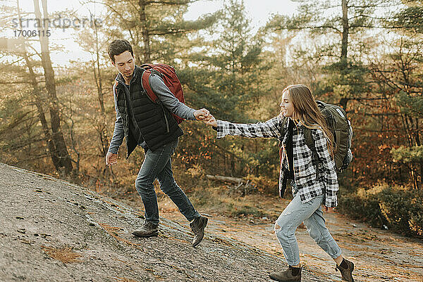Junges Paar hält sich an den Händen  während es bei einer Herbstwanderung einen Hügel hinaufgeht