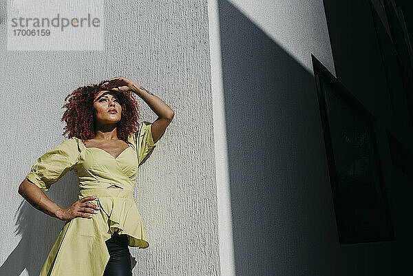 Modische Frau  die ihre Augen abschirmt  während sie an einer Wand an einem sonnigen Tag steht
