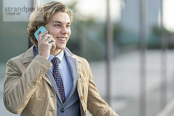 Junger Geschäftsmann lächelt  während er im Freien stehend mit einem Mobiltelefon spricht