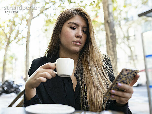 Frau  die ein Mobiltelefon benutzt  während sie in einem Straßencafé in der Stadt Kaffee trinkt