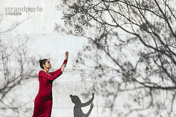 Frau in rotem Kleid mit Tänzerin Pose und Baum Schatten an der Wand