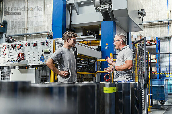 Älterer männlicher Techniker erklärt einem Kollegen eine Maschine in einer beleuchteten Fabrik