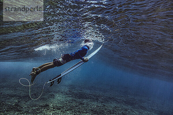 Männlicher Surfer hält Surfbrett beim Tauchen unter Wasser auf den Malediven