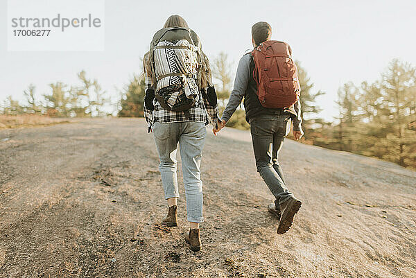 Junges Paar hält sich an den Händen  während es bei einer Herbstwanderung einen Hügel hinaufgeht