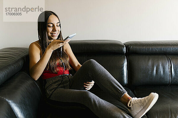 Lächelndes Teenager-Mädchen  das auf dem Sofa zu Hause sitzt und mit dem Handy telefoniert