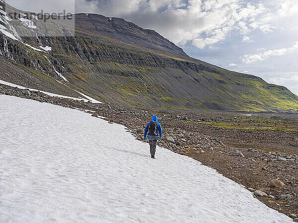 Männlicher Rucksacktourist wandert durch ein verschneites Tal in Richtung Drangajokull-Gletscher
