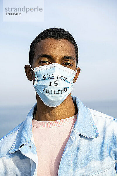 Junger Mann mit Gesichtsmaske mit der Aufschrift Silence Is Violence steht im Freien