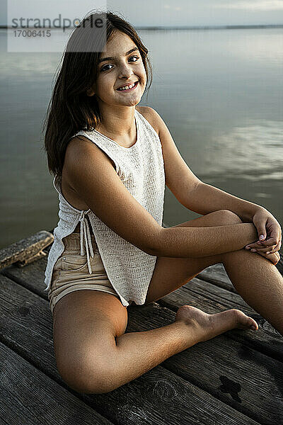 Glückliches Mädchen sitzt auf einem Steg am See