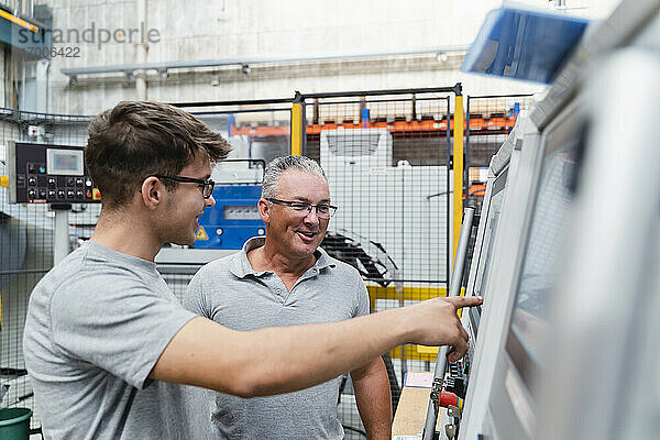 Lächelnde männliche Arbeiter  die eine Maschine in der Industrie untersuchen