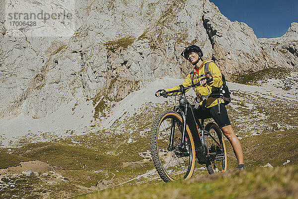 Lächelnde Radfahrerin mit Mountainbike an einem sonnigen Tag im Nationalpark Picos de Europa  Kantabrien  Spanien