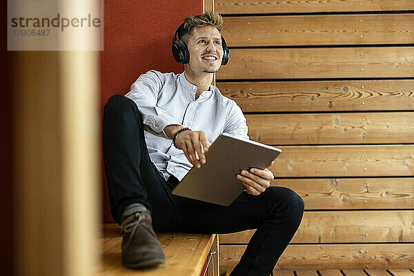 Mann mit Kopfhörern und digitalem Tablet  der wegschaut  während er zu Hause sitzt