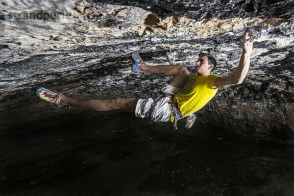 Junge männliche Sportlerin klettert entschlossen in einer Höhle auf einen Felsen