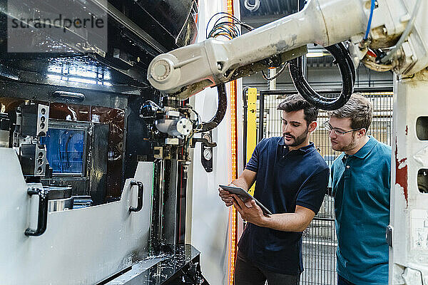 Männliche Mitarbeiter benutzen ein digitales Tablet  während sie in einer Produktionsstätte diskutieren