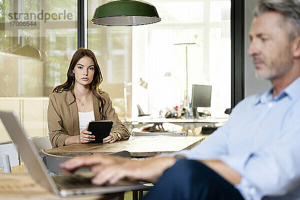 Geschäftsfrau benutzt digitales Tablet  während sie mit einem Kollegen im Büro sitzt