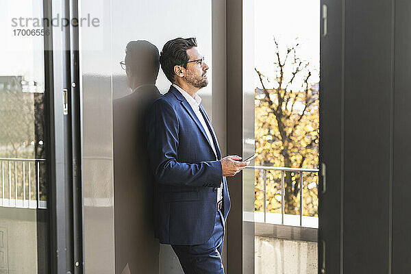 Geschäftsmann  der ein Mobiltelefon benutzt  während er auf dem Balkon eines Büros steht