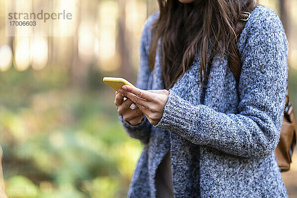 Frau hält Smartphone in der Hand  während sie im Wald von Cannock Chase steht