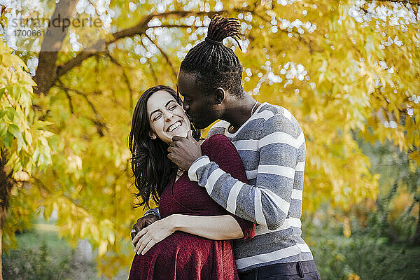 Afrikanischer Mann küsst glückliche schwangere Frau im Park im Herbst
