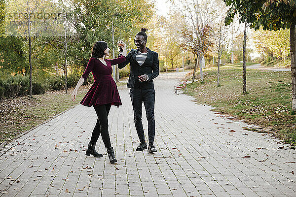 Glückliches multiethnisches Paar tanzt im Park im Herbst