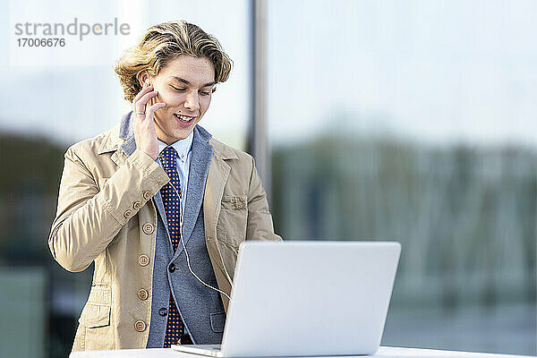 Geschäftsmann passt In-Ear-Kopfhörer an  während er im Freien am Laptop arbeitet