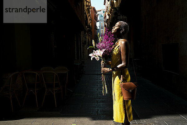 Frau mit geschlossenen Augen  die einen Blumenstrauß hält  steht in der Stadt an einem sonnigen Tag