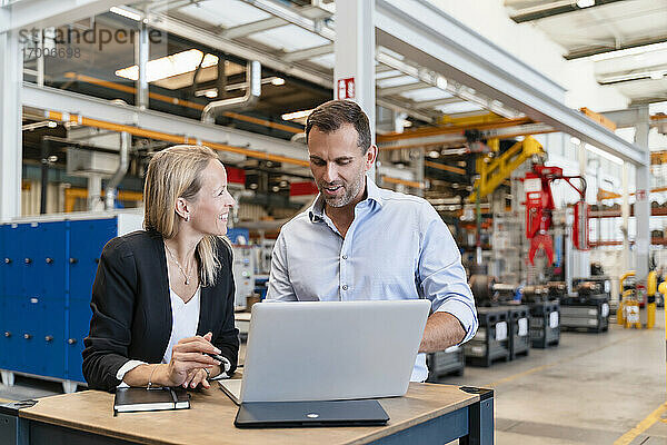 Glückliche männliche und weibliche Kollegen  die in einer Fabrik einen Laptop benutzen