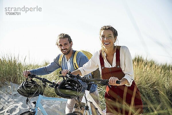 Junger Mann und Frau gehen mit Fahrrädern gegen den klaren Himmel