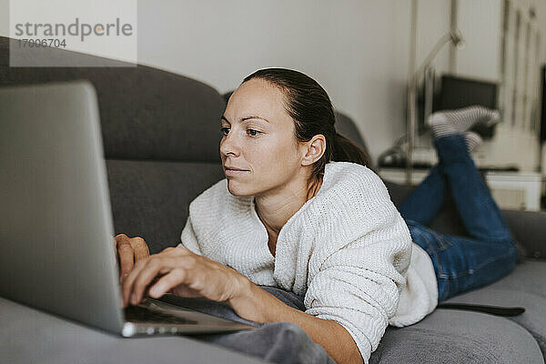 Kaukasische Frau  die einen Laptop benutzt  während sie auf dem Sofa liegt