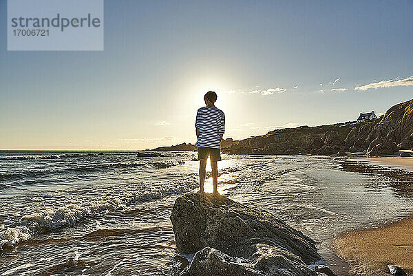 Junge bewundert Meerblick  während er auf einem Felsen am Strand steht