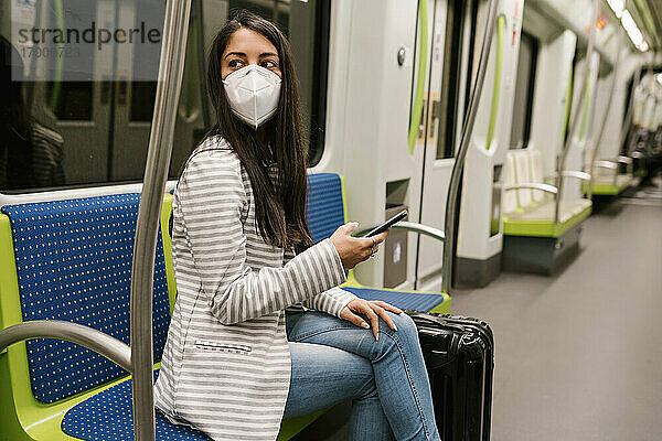 Frau schaut weg  während sie mit ihrem Smartphone in einem U-Bahn-Zug sitzt