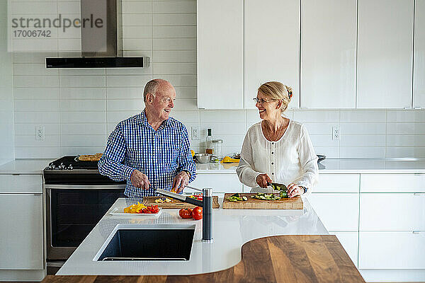 Älteres Paar unterhält sich beim Gemüseschneiden auf der Kücheninsel zu Hause