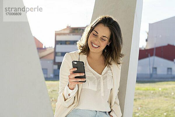 Lächelnde Geschäftsfrau mit Smartphone in der Stadt an einem sonnigen Tag