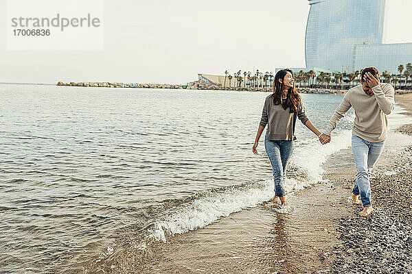 Glückliches junges Paar  das sich bei einem Strandspaziergang gegen den klaren Himmel amüsiert