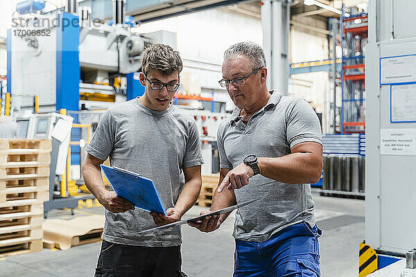 Männliche Mitarbeiter prüfen ein Produkt  während sie in einer beleuchteten Fabrik stehen