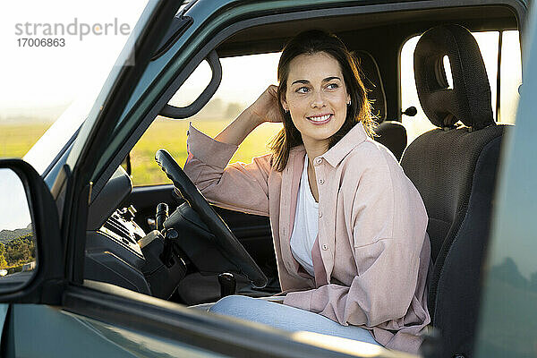 Lächelnde junge Frau  die im Auto sitzend wegschaut  während einer Autoreise