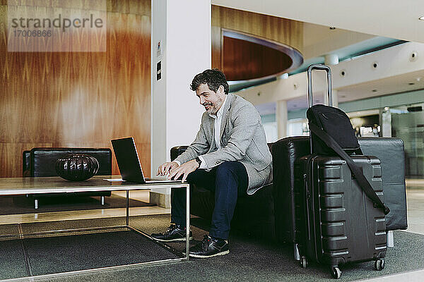 Älterer Geschäftsmann  der einen Laptop benutzt  während er in der Hotellobby sitzt