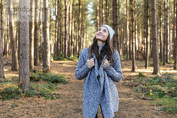 Lächelnde Frau  die beim Winterwandern im Wald von Cannock Chase nach oben schaut