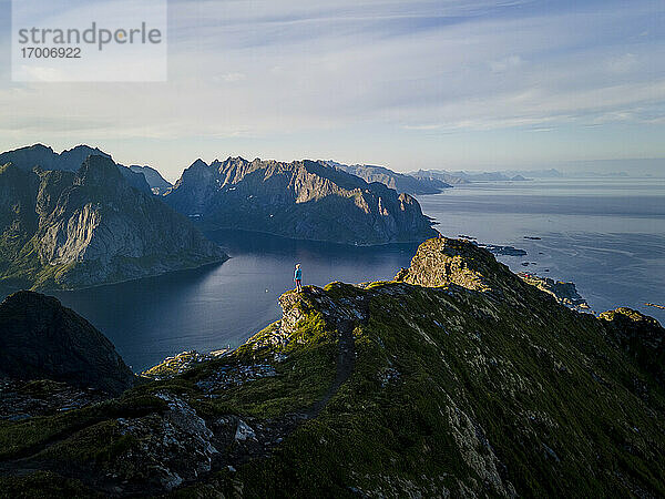 Frau bewundert die Aussicht auf die Berge  während sie auf einem Berg in Reine  Lofoten  Norwegen  steht