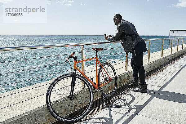 Mann mit Fahrrad auf der Uferpromenade  der sein Smartphone benutzt