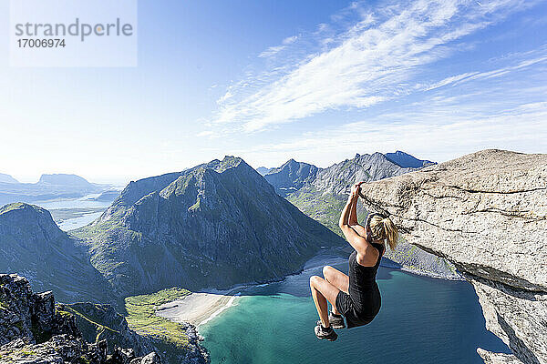 Mittlere erwachsene Frau hängt am Rande eines Berges in Ryten  Lofoten  Norwegen