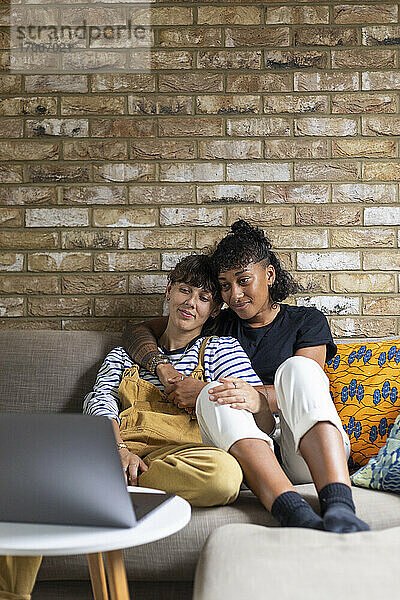 Lesbisches Paar  das zu Hause auf dem Sofa sitzt und den Laptop betrachtet