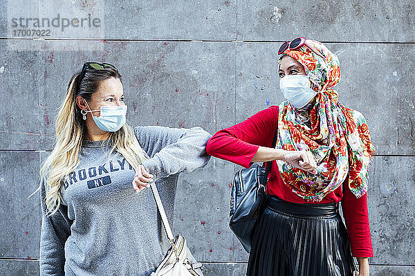 Freundinnen mit Schutzmasken grüßen mit Ellenbogenstößen während der COVID-19