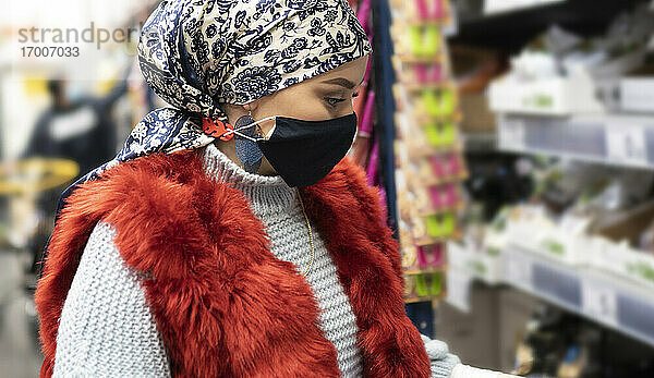 Junge Frau mit Kopftuch und Gesichtsschutzmaske beim Einkaufen im Supermarkt