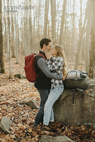 Junges Paar umarmt sich vor einem Felsblock im Wald