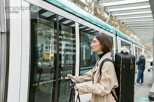 Frau mit Instrumentenkoffer und Elektroroller an der Straßenbahn in der Stadt