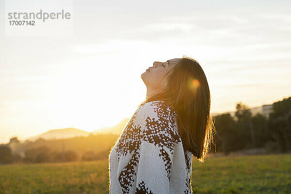 Junge Frau entspannt sich bei Sonnenuntergang mit zurückgelegtem Kopf